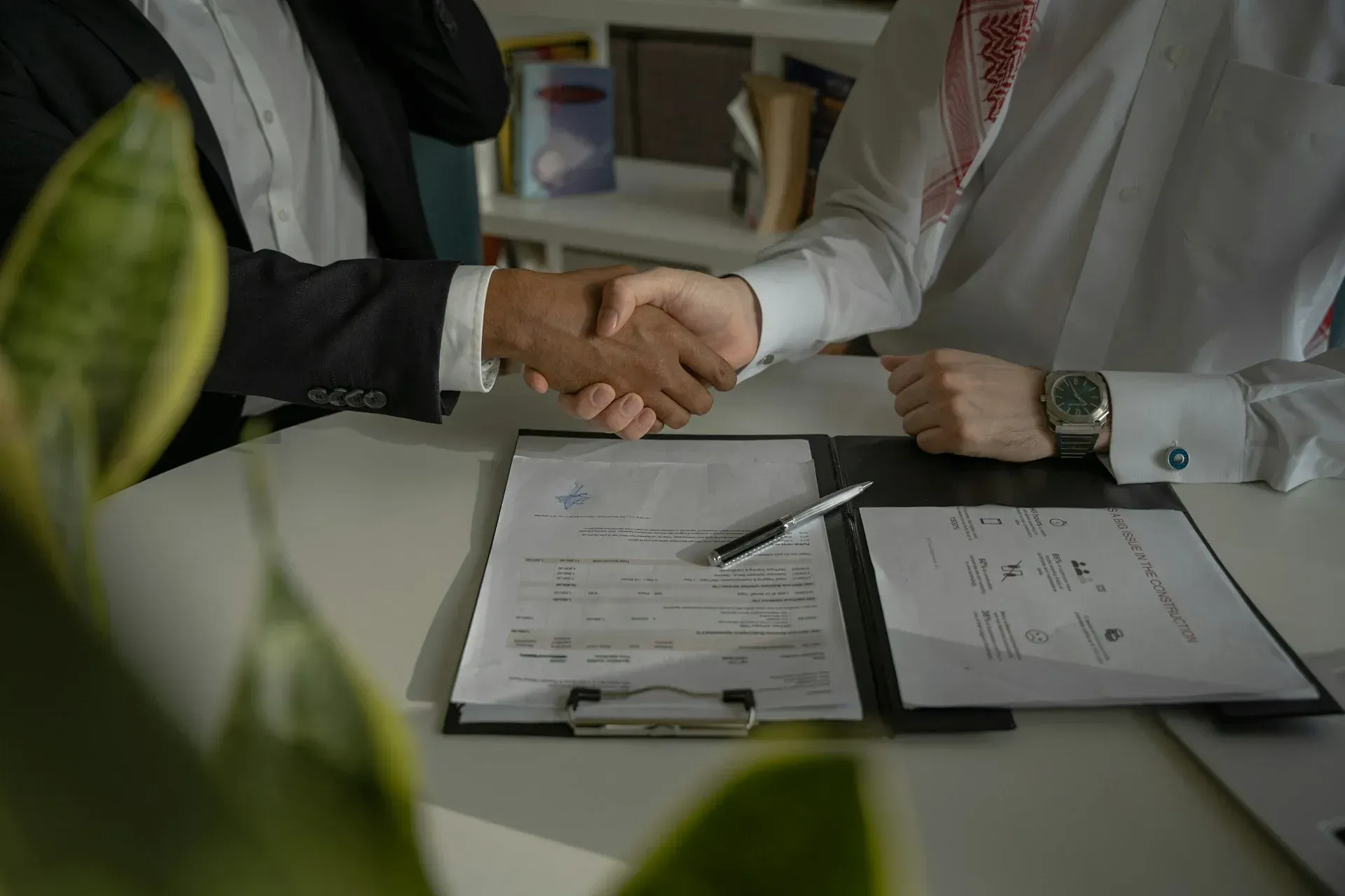 Two men shaking hands over a contract on a desk, possibly a business deal.