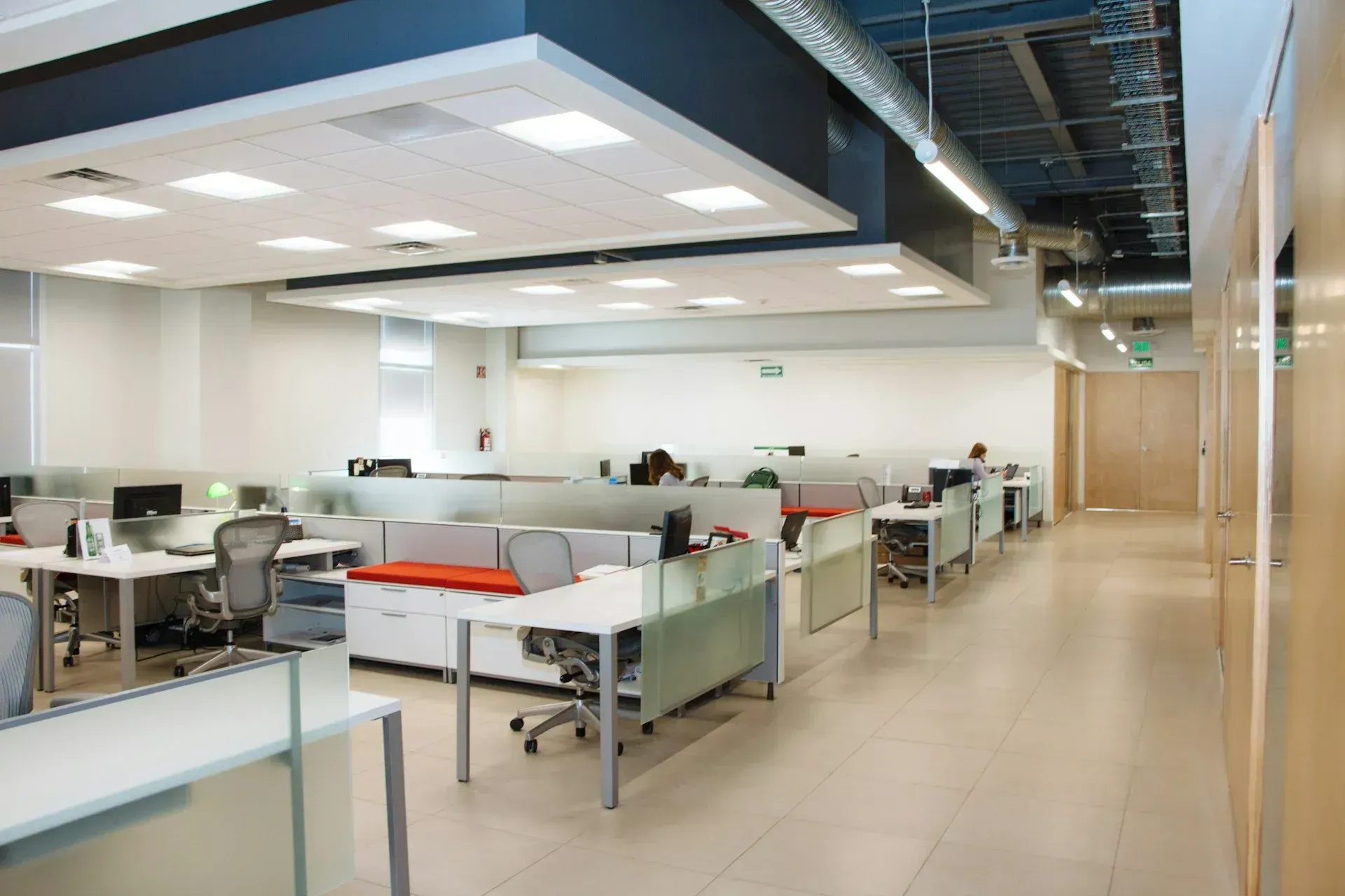 Modern office space with cubicles, white desks, and recessed lighting.